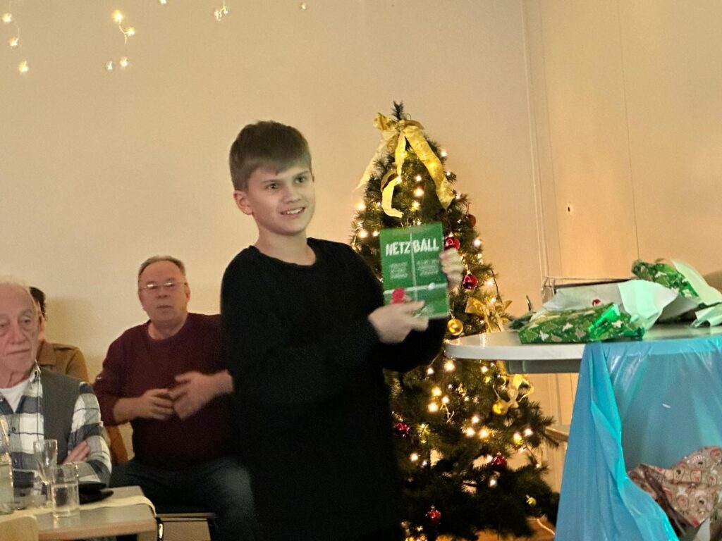 a boy holding a green box in front of a christmas tree